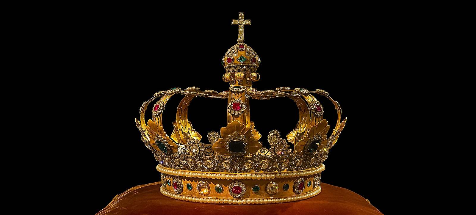 golden bejeweled royal crown on an embroidered red pillow